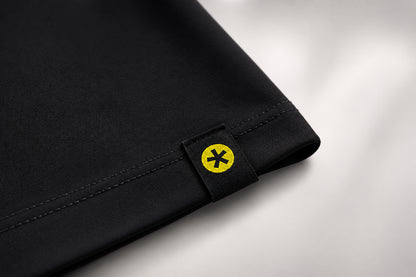 Close-up of a black fabric product corner with a small black tab featuring a yellow circle and black asterisk symbol, set against a light gray background.